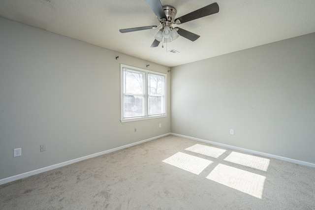 empty room with a textured ceiling, light colored carpet, visible vents, baseboards, and a ceiling fan