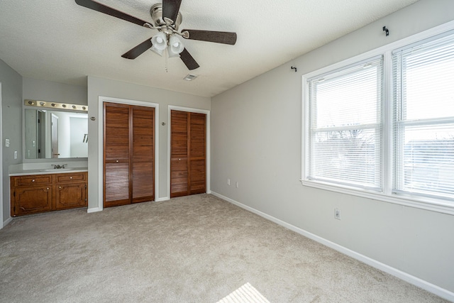 unfurnished bedroom with light carpet, a textured ceiling, two closets, and baseboards