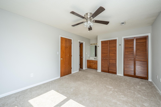 unfurnished bedroom featuring multiple closets, visible vents, light colored carpet, a textured ceiling, and baseboards