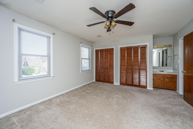 unfurnished bedroom featuring light carpet, a textured ceiling, baseboards, and multiple closets