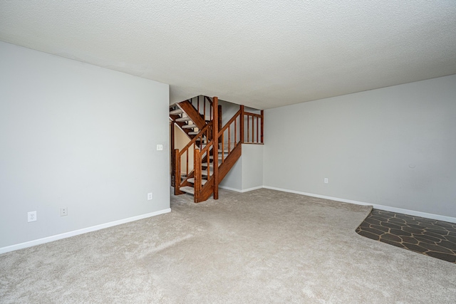 spare room featuring carpet, a textured ceiling, baseboards, and stairs