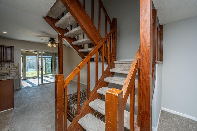 stairway featuring a textured ceiling, carpet, a ceiling fan, and baseboards