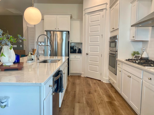 kitchen with appliances with stainless steel finishes, hanging light fixtures, white cabinetry, wall chimney exhaust hood, and light hardwood / wood-style flooring