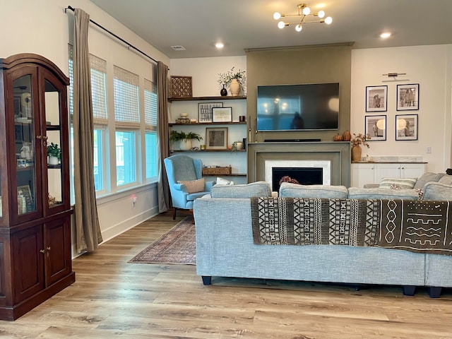 living room featuring an inviting chandelier, light hardwood / wood-style flooring, and a premium fireplace