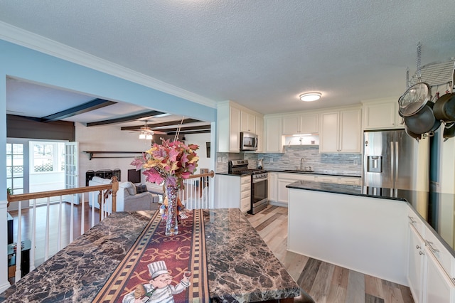 kitchen with a brick fireplace, beamed ceiling, light hardwood / wood-style floors, white cabinets, and appliances with stainless steel finishes