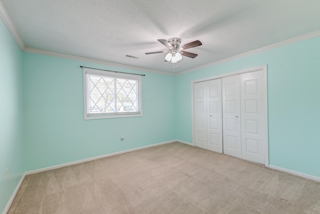 unfurnished bedroom featuring light carpet, a textured ceiling, ceiling fan, crown molding, and a closet