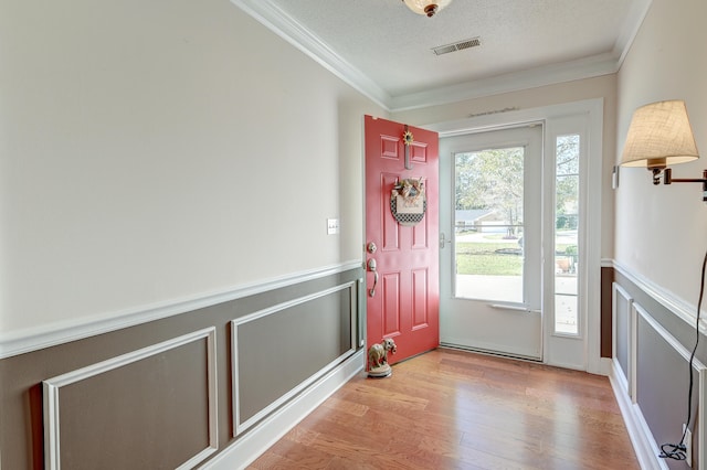 doorway to outside with a textured ceiling, crown molding, and light hardwood / wood-style flooring