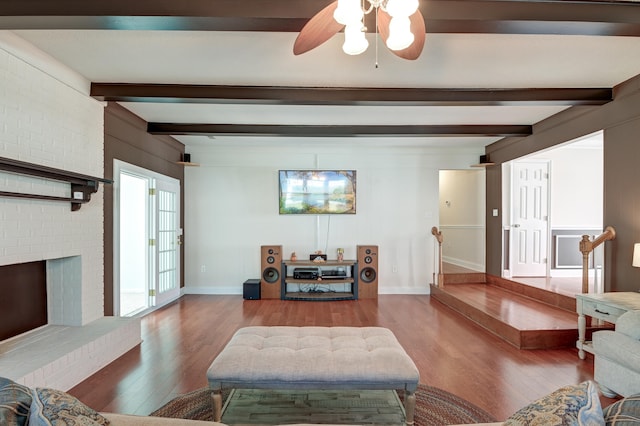 living room featuring beamed ceiling, ceiling fan, wood-type flooring, and a brick fireplace