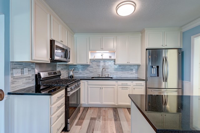 kitchen with appliances with stainless steel finishes, dark stone counters, sink, light hardwood / wood-style flooring, and white cabinetry