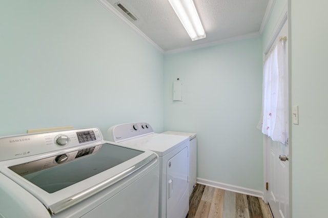 laundry room with a textured ceiling, light hardwood / wood-style floors, washer and clothes dryer, and ornamental molding