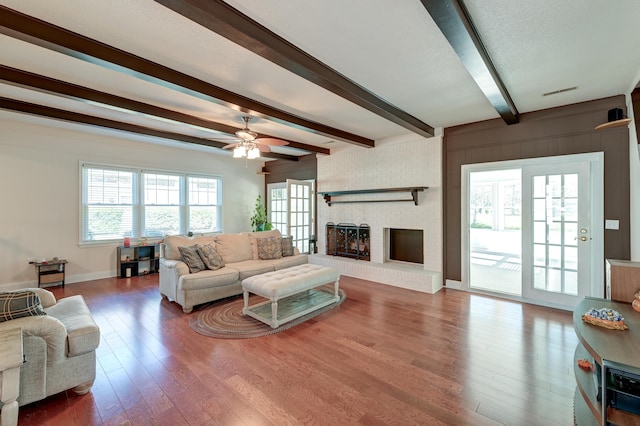 living room featuring beamed ceiling, hardwood / wood-style floors, a brick fireplace, and plenty of natural light