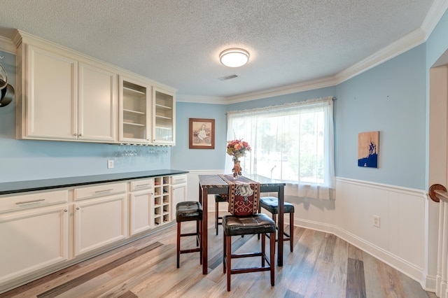 dining area with a textured ceiling, light hardwood / wood-style floors, and ornamental molding