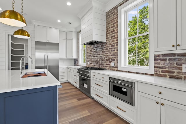 kitchen with high end appliances, sink, white cabinets, and decorative light fixtures