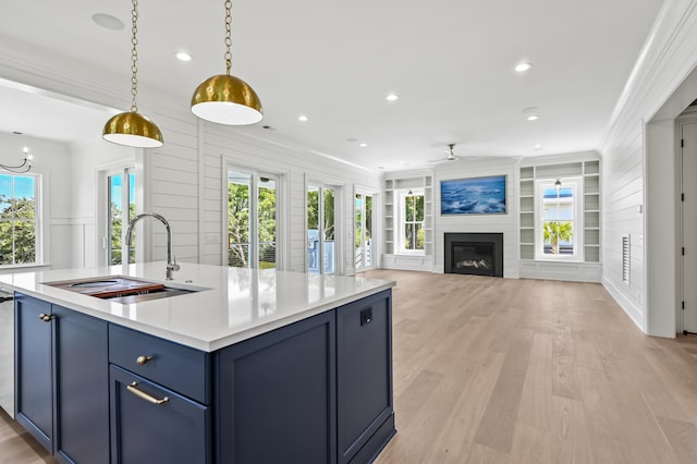 kitchen featuring blue cabinetry, sink, decorative light fixtures, a center island with sink, and a large fireplace