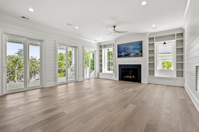 unfurnished living room with wooden walls, a fireplace, light hardwood / wood-style flooring, ceiling fan, and built in shelves