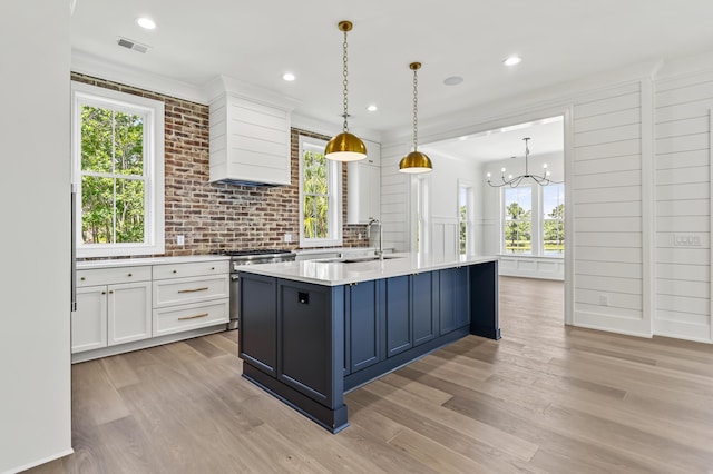 kitchen with pendant lighting, sink, stainless steel stove, white cabinetry, and custom exhaust hood