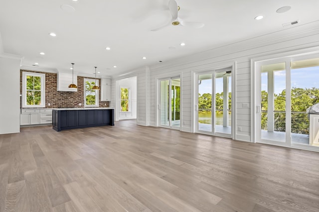 unfurnished living room featuring crown molding, a wealth of natural light, ceiling fan, and light wood-type flooring