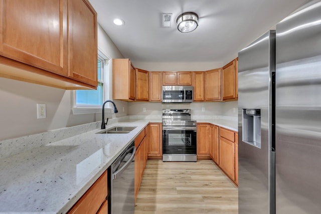 kitchen with light stone countertops, sink, appliances with stainless steel finishes, and light hardwood / wood-style floors