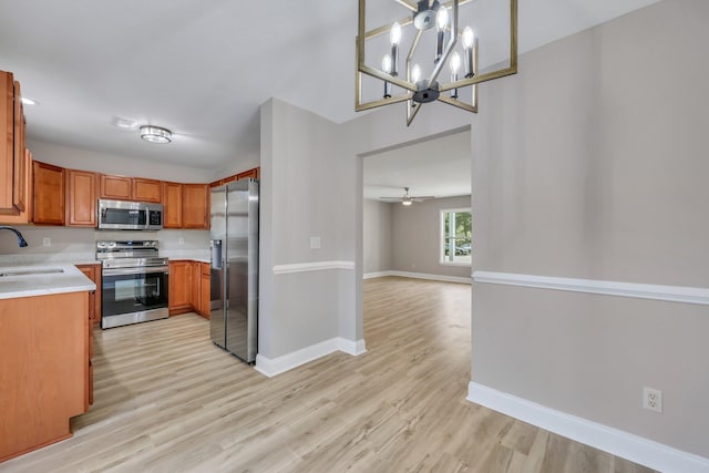 kitchen with ceiling fan with notable chandelier, sink, appliances with stainless steel finishes, and light wood-type flooring