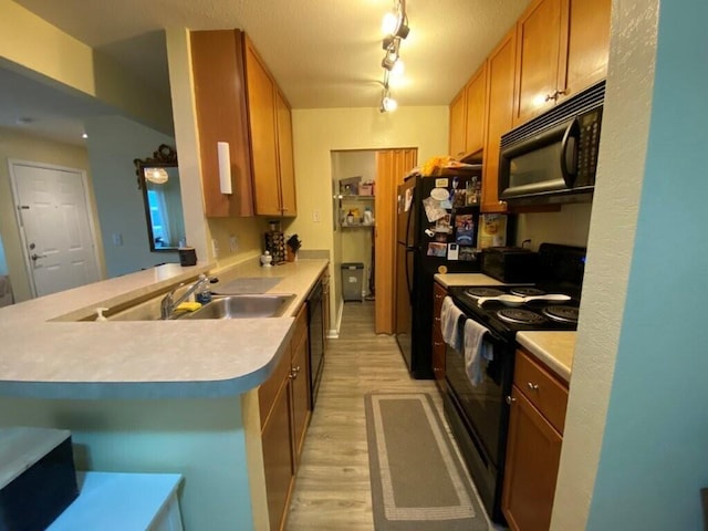 kitchen with light wood-type flooring, light countertops, a peninsula, black appliances, and a sink