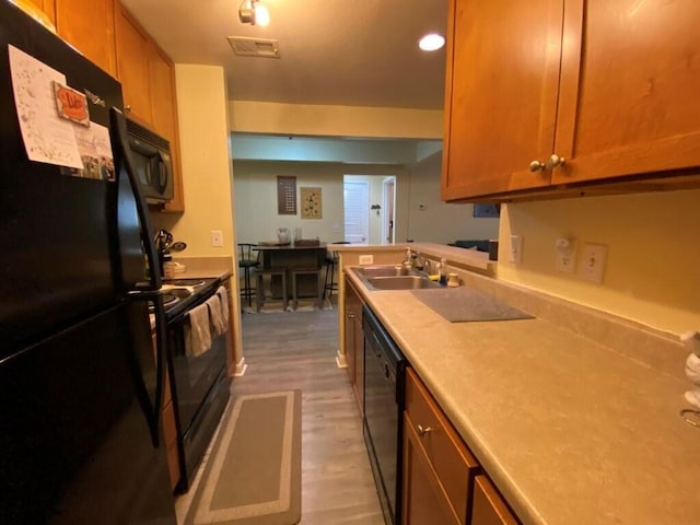 kitchen featuring visible vents, black appliances, a sink, light wood finished floors, and light countertops