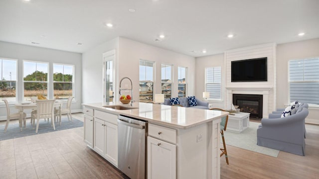 kitchen with dishwasher, a sink, light wood finished floors, a kitchen island with sink, and white cabinetry