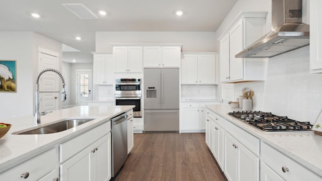 kitchen with appliances with stainless steel finishes, wall chimney range hood, a sink, white cabinetry, and recessed lighting
