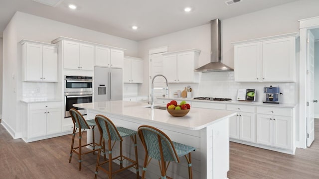 kitchen featuring wall chimney exhaust hood, white fridge with ice dispenser, a sink, gas cooktop, and a center island with sink