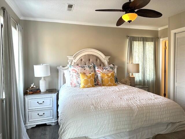 bedroom with visible vents, a textured ceiling, ornamental molding, and dark wood-type flooring