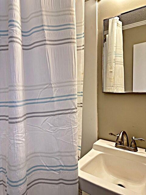 full bath featuring a textured ceiling, a sink, and crown molding