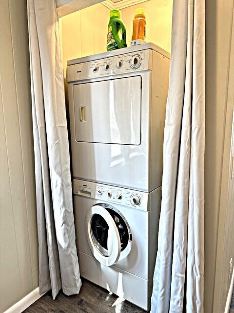 clothes washing area featuring stacked washer and dryer, dark wood-type flooring, wood walls, and laundry area