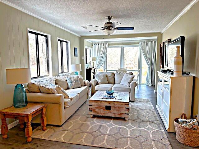 living area featuring a textured ceiling, ornamental molding, light wood-style flooring, and a ceiling fan