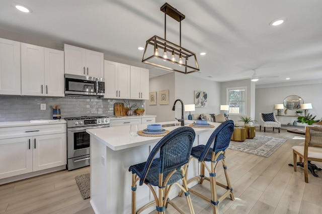 kitchen featuring light countertops, white cabinets, stainless steel appliances, tasteful backsplash, and open floor plan
