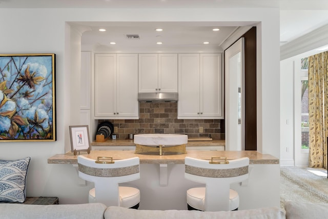32 Prioleau St Unit J, Charleston, SC 29401 - kitchen featuring under cabinet range hood, decorative backsplash, a breakfast bar, light countertops, and white cabinets