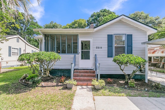 2215 Suffolk St, North Charleston, SC 29405 - view of front facade with entry steps, a chimney, a front lawn, and a sunroom