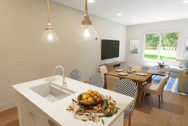 kitchen featuring open floor plan, pendant lighting, light wood finished floors, and a sink