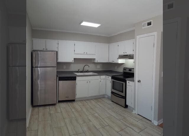 kitchen with stainless steel appliances, a sink, under cabinet range hood, dark countertops, and white cabinetry