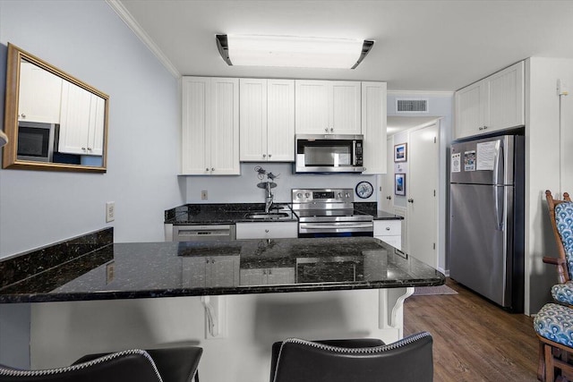 kitchen with dark hardwood / wood-style flooring, crown molding, stainless steel appliances, kitchen peninsula, and dark stone countertops