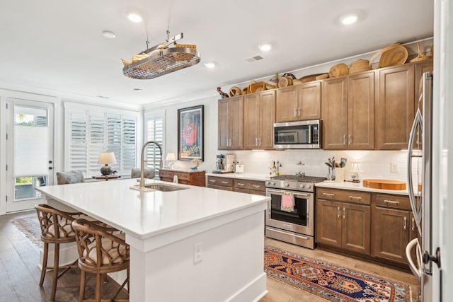 kitchen with light hardwood / wood-style floors, a breakfast bar area, an island with sink, sink, and stainless steel appliances