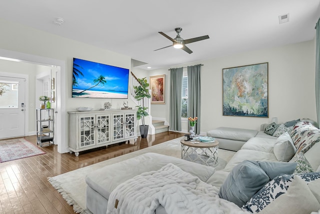 living area with ceiling fan, wood finished floors, visible vents, baseboards, and stairway