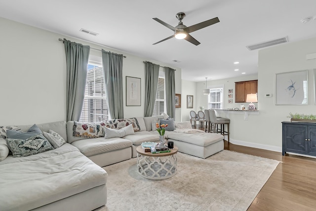 living area with visible vents, ceiling fan, baseboards, and wood finished floors