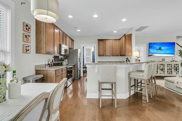 kitchen with stainless steel appliances, brown cabinets, a kitchen bar, and hardwood / wood-style flooring