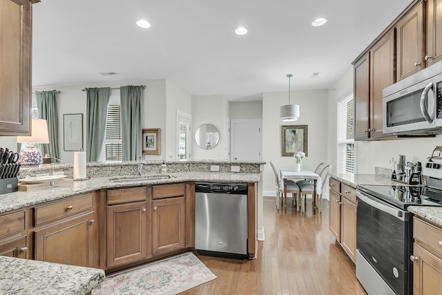 kitchen with stainless steel appliances, light wood-type flooring, a sink, and light stone countertops