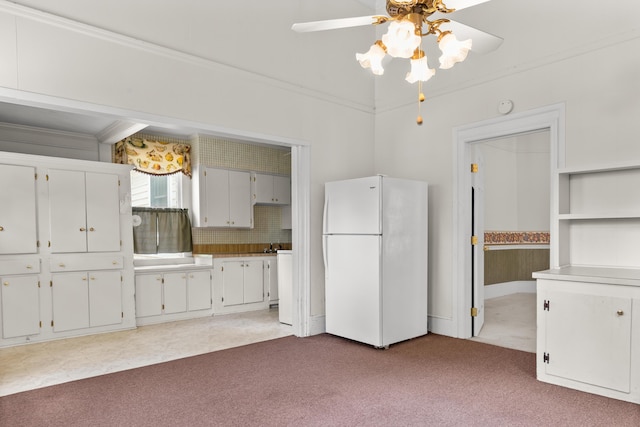 kitchen featuring freestanding refrigerator, a ceiling fan, carpet, crown molding, and white cabinetry