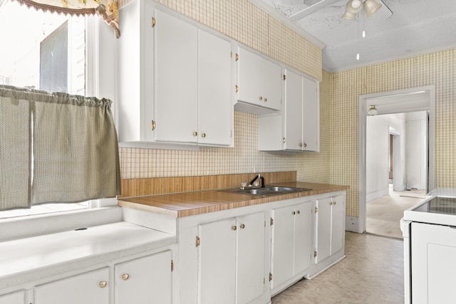 kitchen with white range with electric cooktop, a sink, wallpapered walls, light floors, and white cabinetry