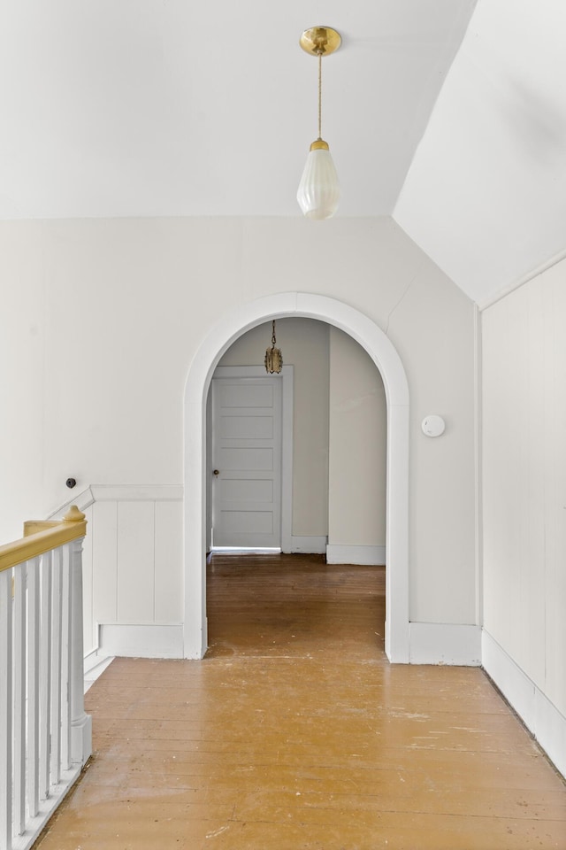 hall with arched walkways, light wood finished floors, and vaulted ceiling
