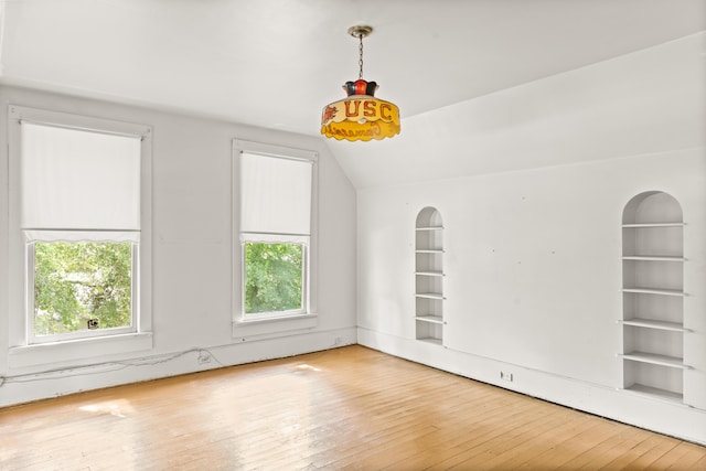 empty room featuring healthy amount of natural light, hardwood / wood-style floors, lofted ceiling, and built in shelves