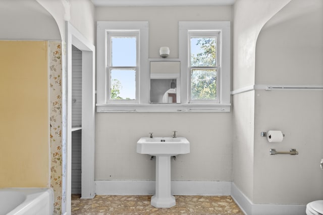 bathroom featuring healthy amount of natural light, toilet, and a bath