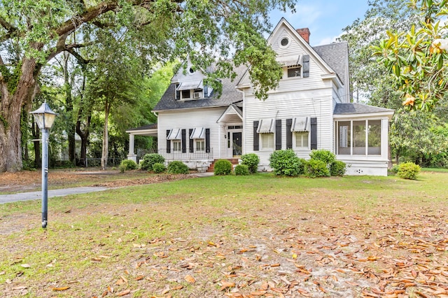 view of front of house with roof with shingles, a chimney, a front yard, and a sunroom