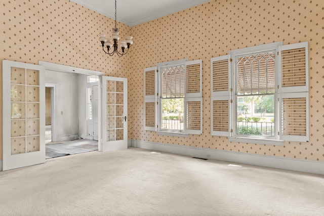 carpeted spare room with healthy amount of natural light, a chandelier, ornamental molding, and wallpapered walls